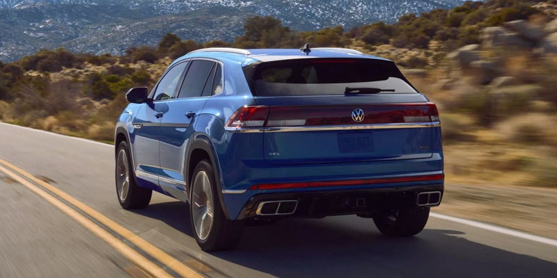 Blue 2026 Volkswagen Atlas Cross Sport driving on a scenic mountain highway.