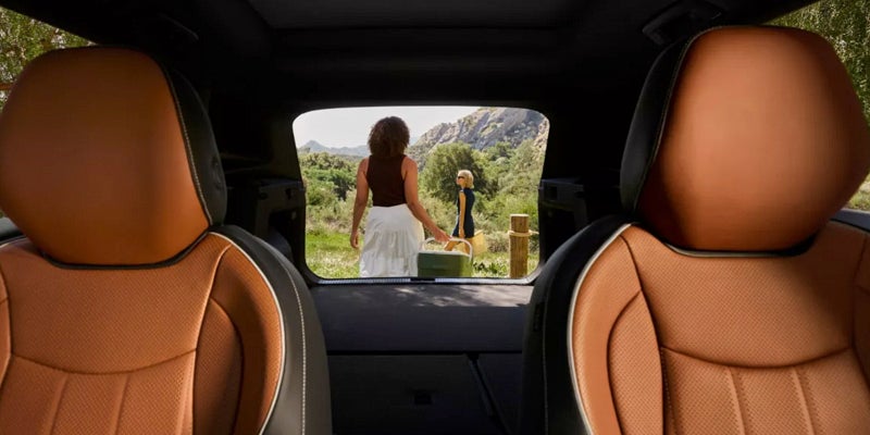 View from inside a 2026 Volkswagen Tiguan cargo area showing brown leather seats and two people outside near a scenic mountain landscape.